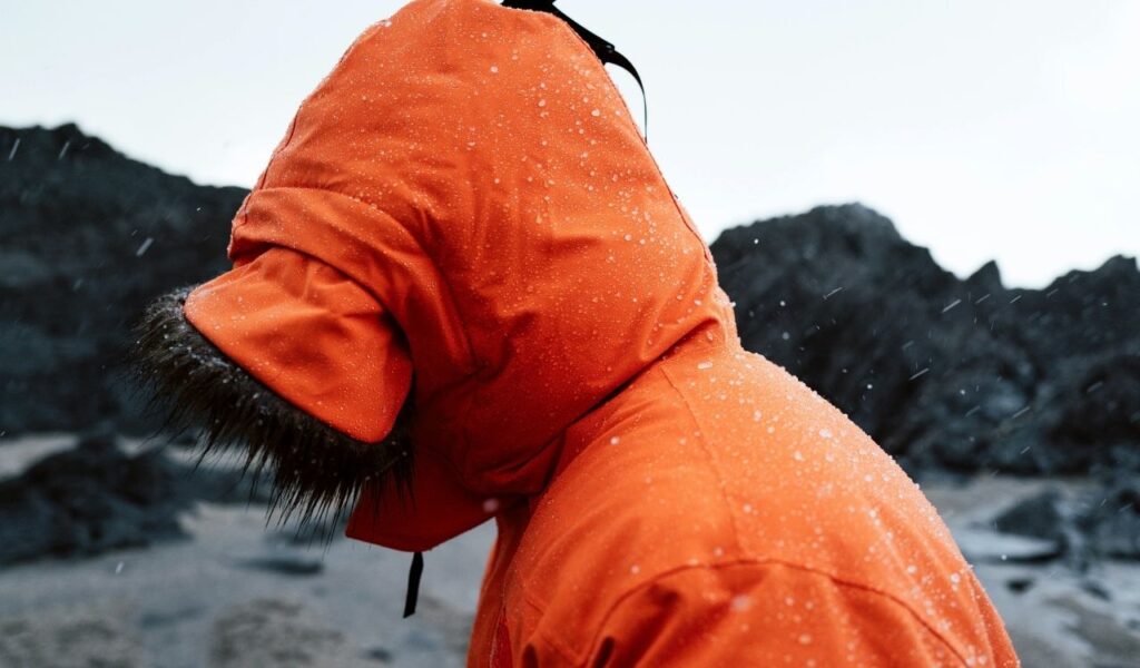 Person Wearing a Warm, Orange Jacket with a Hood on a Beach on a Rainy Day